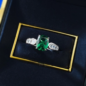 Macro shot of an emerald-cut green gemstone ring with side baguette diamonds in a box