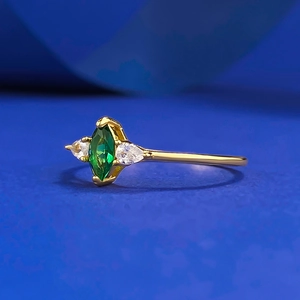Elegant gold marquise emerald ring with pear-cut side diamonds on a blue background