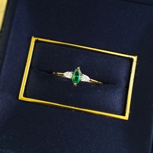 Macro detail of marquise green emerald ring with pear side stones in gold setting