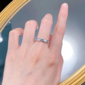 Detailed view of silver heart-shaped band ring with blue stones worn on a finger
