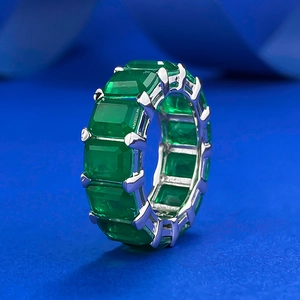 Eternity ring with emerald-cut green gemstones set in 925 silver on a blue background