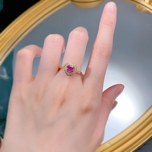 Macro detail of a 925 silver heart-shaped pink gem ring with gold finish on a finger