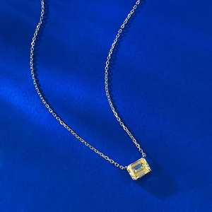Close-up of radiant yellow cushion cut stone necklace pendant on a navy textured background