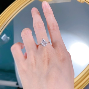 Close-up of a pear-cut white stone ring on finger with polished silver band detail