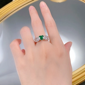Gros plan d'une bague émeraude en forme de cœur portée au doigt avec accents diamants