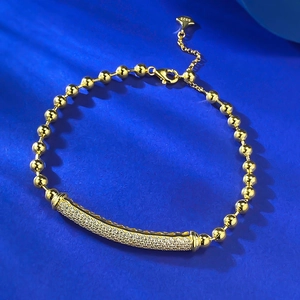 Golden bead bracelet with sparkling zircon tube on deep blue textured background