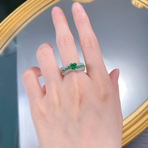 Close-up of heart-shaped emerald ring with wavy pave band on hand model