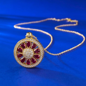 Golden flower pendant necklace featuring red pear-cut gems and white crystals on blue background