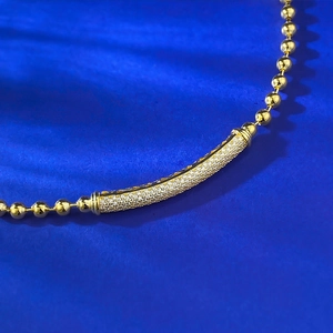 Macro shot of gold beaded bracelet with a curved tube sparkling in pave white diamonds