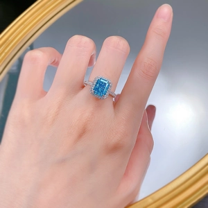 Macro detail of radiant cut blue gemstone ring with halo diamonds on a hand