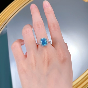 Detailed shot of a halo-set rectangular blue diamond engagement ring worn on a hand