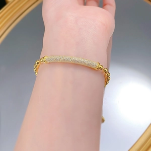 Close-up of a gold beaded bracelet with a sparkling crystal-encrusted tube on a wrist