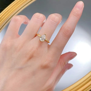 Close-up of a pear-cut white stone ring in gold on a model finger with a mirror background