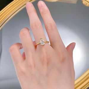 Close-up of a pear-cut white crystal ring in gold finish worn on a model's hand