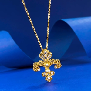 Macro shot of gold iris flower pendant with hollow filigree and white crystals on blue silk