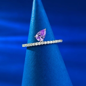 Close-up of a pear-cut purple gemstone ring with a diamond-paved band on a blue stand