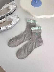 Detail of grey crew socks featuring green bow embroidery and checkered ruffle cuffs