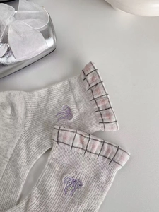 Macro detail of sheer mesh socks featuring purple bow embroidery and plaid trim accents