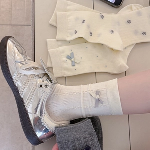 Detail of white ribbed cotton crew socks with bow knot paired with silver metallic sneakers