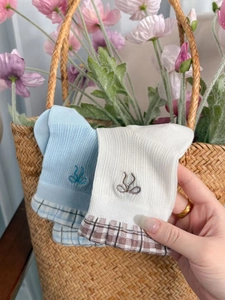 Detail of knitted mid-calf socks featuring bow embroidery and checkered cuffs in soft pastel tones