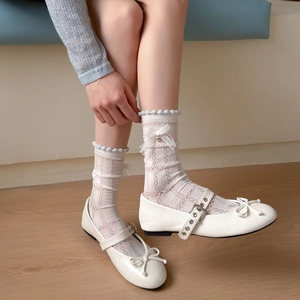 Close-up of white Mary Jane flat shoes with lace socks featuring pearl bows and textures