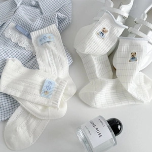Detail of white cotton mid-calf socks with cute bear embroidery and artistic blue fabric label