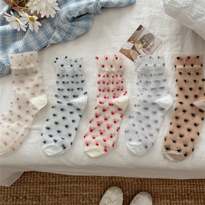 Detail of sheer glass silk socks with heart patterns and ruffle cuffs on white linen