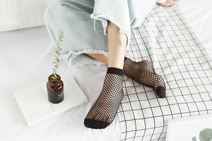 Detail of black hollow fishnet ankle socks with wide mesh pattern on female feet