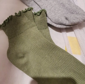 Close-up of grass green crew socks featuring ruffled lace cuffs and ribbed cotton texture