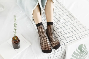 Detail of black fishnet socks with ribbed cuffs and reinforced toes on white bed