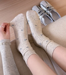 Detail of beige cotton mid-calf socks with blue floral print and ribbed texture on feet