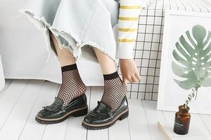 Detail of black fine mesh fishnet socks paired with dark green tassel platform loafers