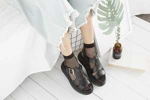 Detail of black open-toe fishnet socks worn with strappy platform sandals and denim