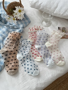 Detail of sheer mesh crew socks featuring five colorful heart patterns on a white bed