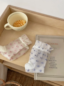 Detailed view of sheer mesh crew socks with polka dots and ruffled cuffs on wooden tray