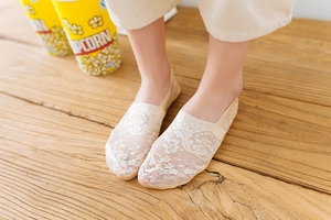 Detailed view of floral lace no-show socks in beige on a textured wooden floor