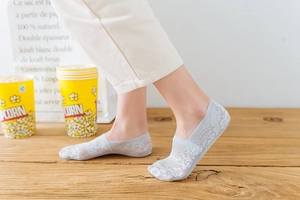 Detail of gray floral lace boat socks on feet with a light wood background for summer