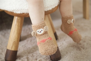 Close-up of brown coral fleece baby socks with a 3D cartoon monkey embroidery detail