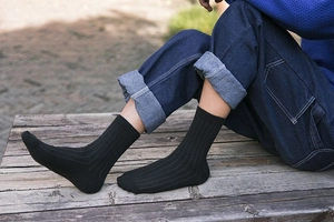 Detail of black ribbed wool business socks shown on a model sitting on a wooden bench