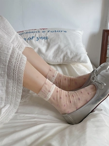 Detail of sheer beige socks with pink polka dots and silver bow flats on a bed