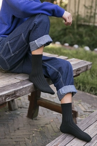 Detail of black ribbed wool socks for men styled with denim jeans on a wooden bench