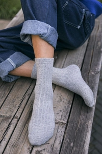 Detail of grey ribbed wool blend socks worn with jeans on a rustic wooden bench