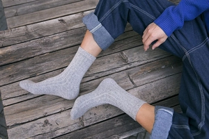 Close-up of gray wool socks with rib knit texture worn with jeans on a wooden deck