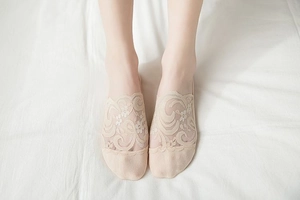 Close-up of beige floral lace no-show socks with reinforced toe on soft white fabric