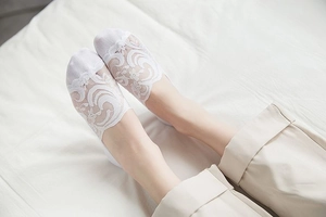 Detail of white lace invisible boat sock with floral pattern on female feet