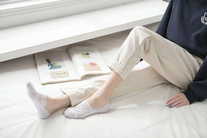 Close-up of white floral lace low cut invisible boat socks worn with casual light pants