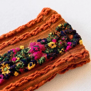 Close-up of orange cable knit sock featuring vintage colorful floral embroidery detail