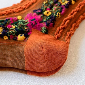 Detailed close-up of vintage cable knit texture and colorful floral embroidery on cotton socks
