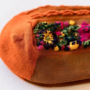 Close-up of vintage floral embroidery and knit cable textures on orange autumn socks
