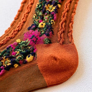 Macro view of cable-knit texture and vintage floral patterns on warm orange winter socks